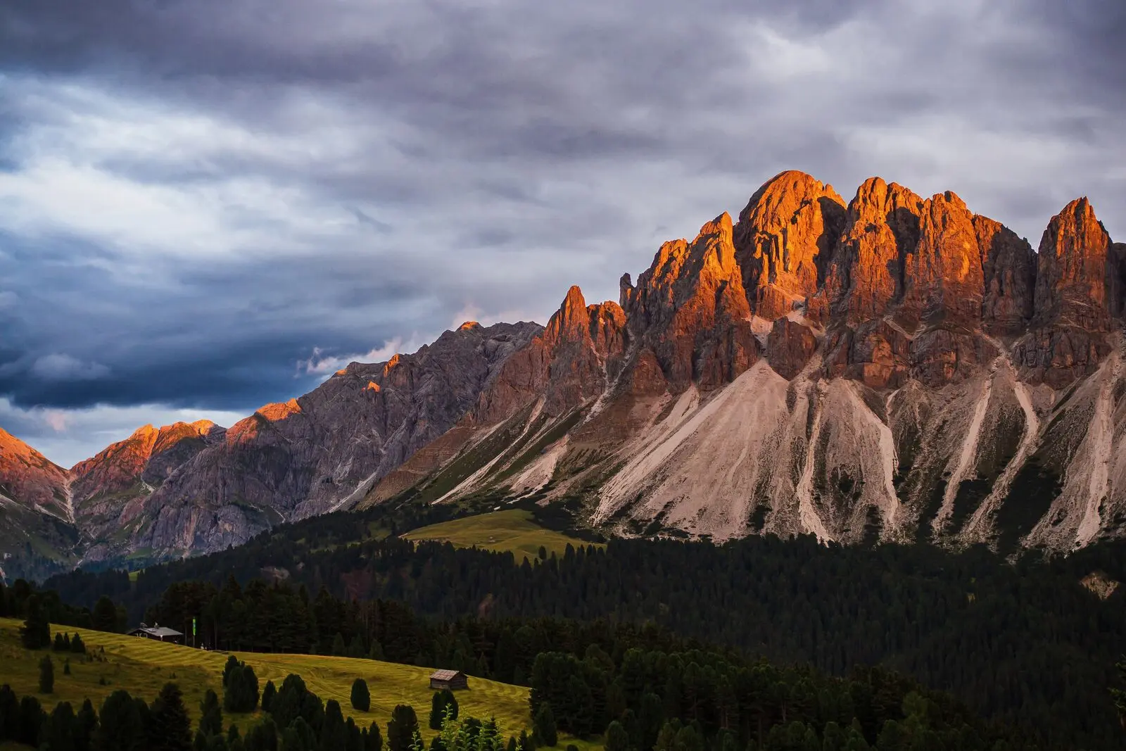 Alpenglow on a Dolomites rock face under heavy clouds