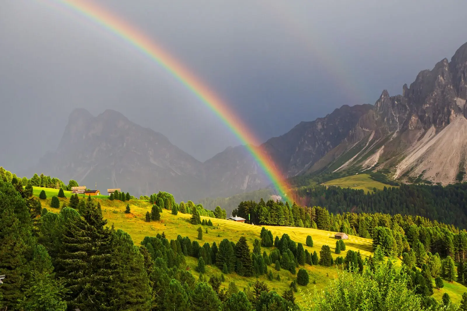 A rainbow over green alpine meadows below jagged peaks