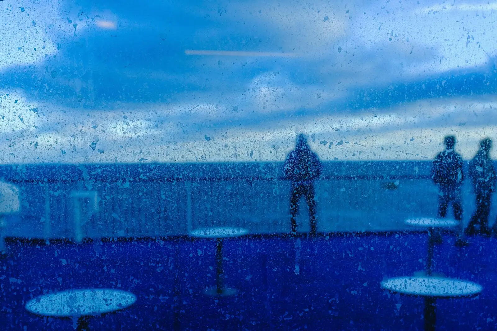 Figures behind rain-covered glass in deep blue