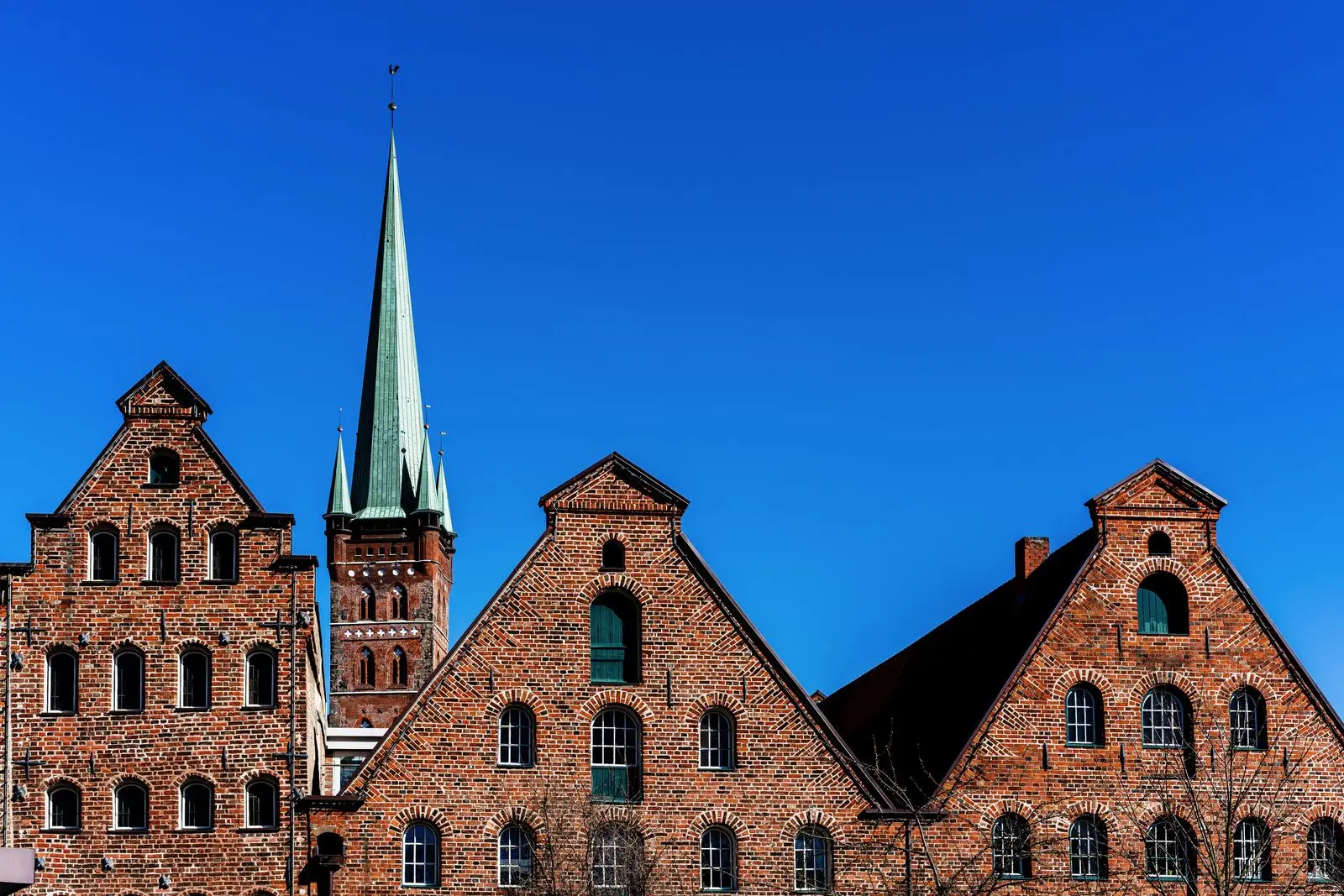 The brick gables of Lübeck’s Salzspeicher and a church spire under a deep blue sky